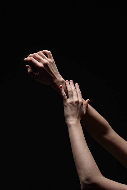 istock Artistic composition of two feminine hands in a delicate pose against a deep black background, highlighting natural form and subtle lighting 2254569275