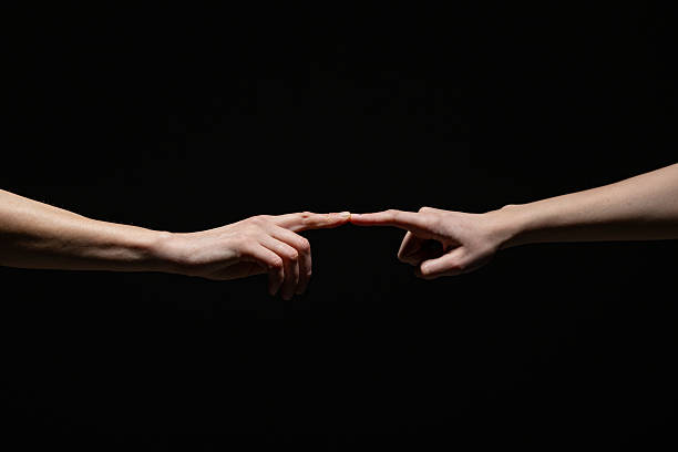istock Two outstretched hands gently connect at the fingertips, evoking a sense of creation, unity, or intimacy against a deep black background with copy space 2254569300