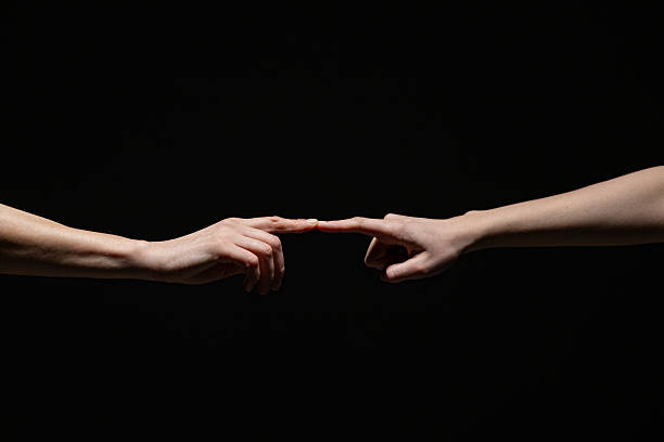 istock Two outstretched hands gently connect at the fingertips, evoking a sense of creation, unity, or intimacy against a deep black background with copy space 2254569306
