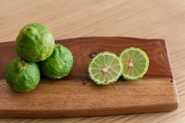 Fresh bergamot limes placed on wooden board, with one sliced open showing juicy interior and seeds.