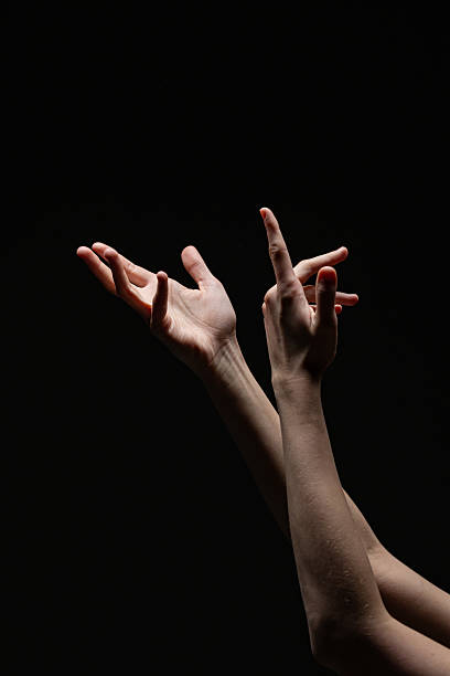 Two feminine hands extend upward in a fluid, expressive gesture, softly lit against a black background. A minimalist, dramatic visual ideal for artistic themes