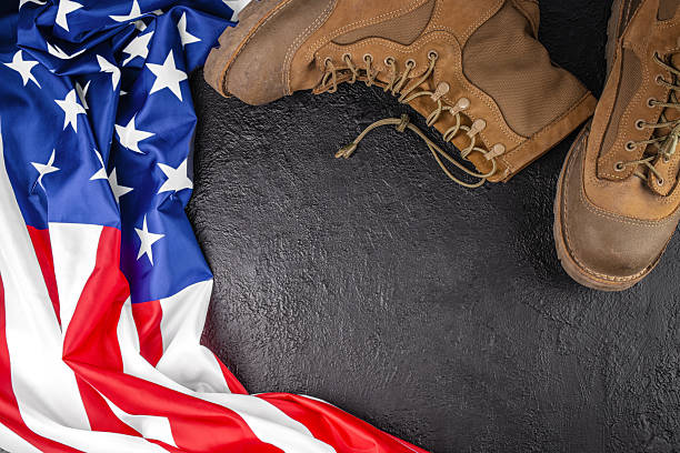 Top view of US military boots and American flag on dark textured background with large copy space, patriotic army and veterans concept for banner and advertising design