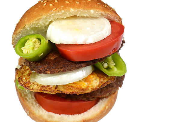 a large stacked hamburger, grilled ground meat beef patty, served in a sesame bun, with thick cuts of tomatoes, white onions and slices of green peppers and fried egg, fast junk food concept