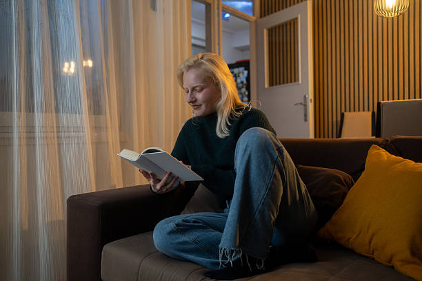 istock Woman sitting on comfy couch reading a book 2254576416