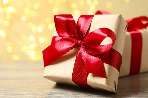 istock Wrapped gifts with red ribbons on table with bright bokeh behind 2254577072