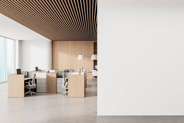 istock Modern office interior with wooden desks and slatted ceiling featuring a large empty white wall for poster or canvas mockup presentation on the right.. 3D Rendering 2254579292