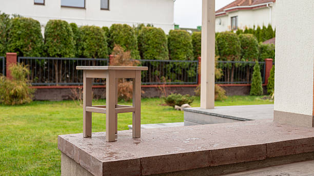 Wooden stool on stone patio with green backyard and hedge.