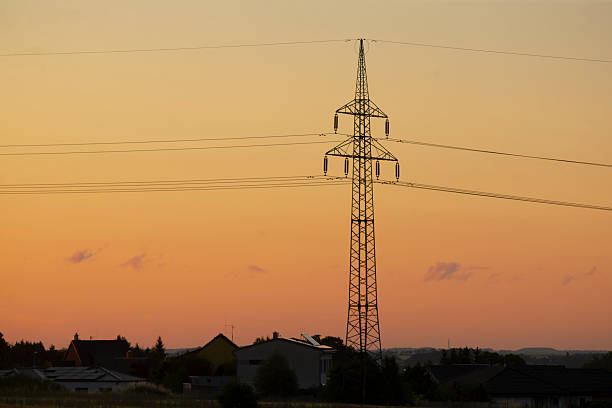 sunset over rural field with pylon, utility technician imagined inspecting transmission lines, warm orange sky, long cables stretching to horizon, distant houses and calm meadow,
