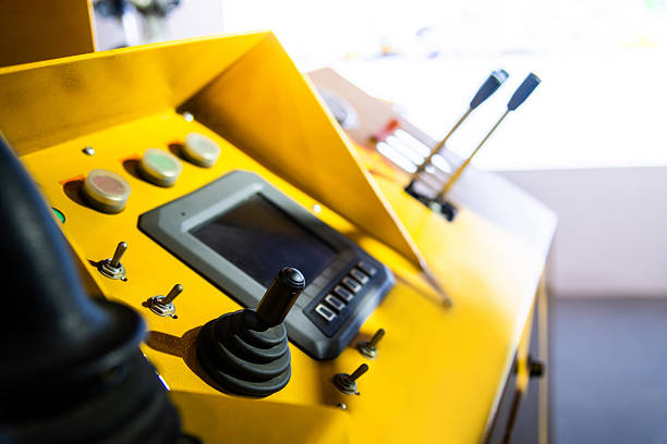 A young woman worker operates industrial equipment on the job, wearing safety gear.  Confident safe worker in her work place.  She smiles, enjoying her work.