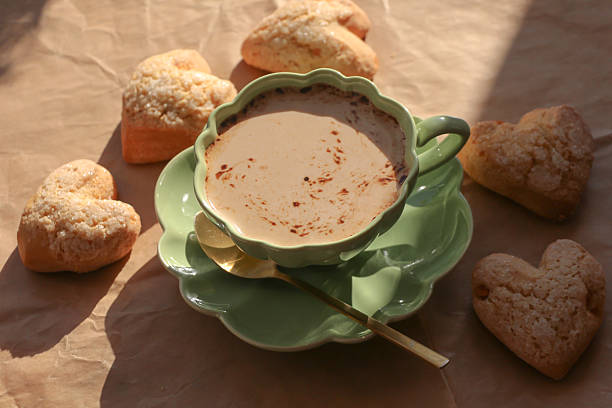 Hot Coffee with Milk in Green Cup Surrounded by Heart Shaped Cookies