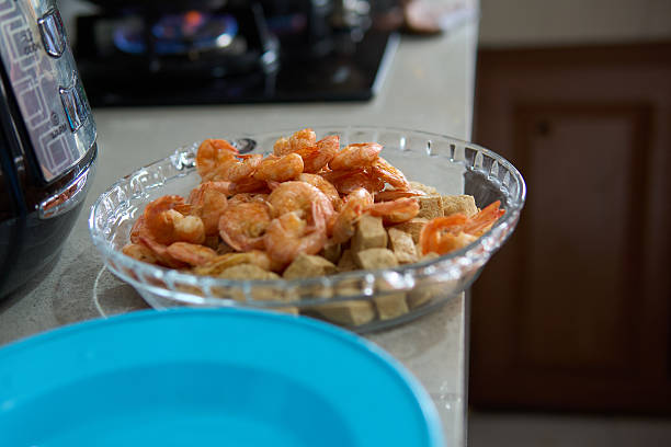 Raw shrimp and tofu displayed in a glass bowl on a kitchen surface, symbolizing fresh ingredients and home cooking preparation.