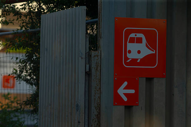close up train icon arrow sign pointing to platform, commuter scanning route, temporary fencing on station approach, evening glow and industrial textures frame urban transit scene