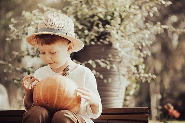 Toddler boy decorating pumpkins on the porch. He is dressed in fall outdoor casual clothes. Exterior of porch at private home in Toronto, Canada.