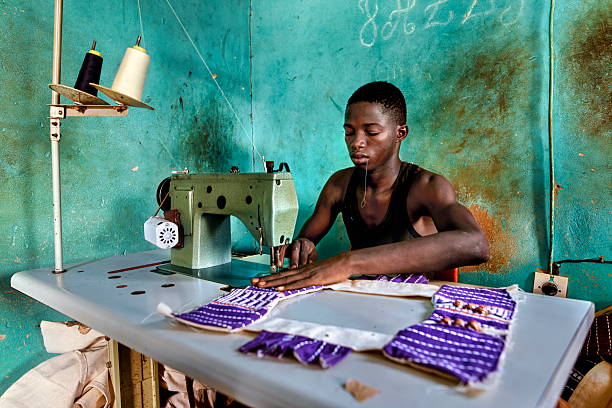 istock Young african man sewing fabric with sewing machine in a poor village 2254595049