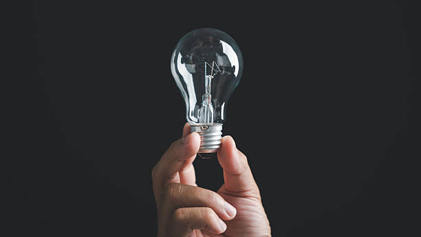 istock Hand holding a lightbulb against a black background. Concept of ideas, innovation, and solutions. 2254595578