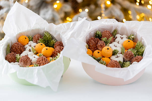 Zephyr arrangement featuring pine cones, cotton bolls, and oranges nestled in white tissue paper, creating a festive atmosphere with natural elements and seasonal charm