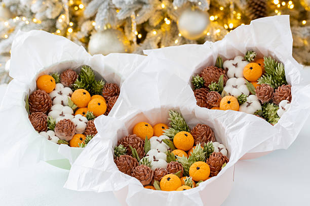 Zephyr arrangement featuring pine cones, cotton bolls, and oranges nestled in white tissue paper, creating a festive atmosphere with natural elements and seasonal charm