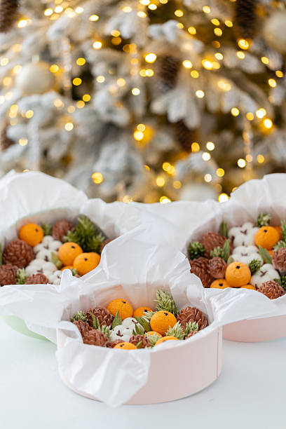 Zephyr arrangement featuring pine cones, cotton bolls, and oranges nestled in white tissue paper, creating a festive atmosphere with natural elements and seasonal charm