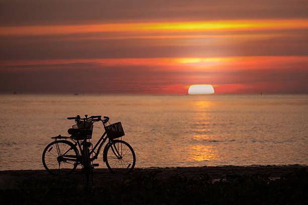Image of the sun setting over the sea. Silhouette of a bicycle parked by the sea against the backdrop of a bright evening sky before dusk.