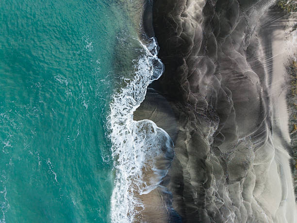 istock Waves crash onto the shore at a beach with dark sand and clear water under bright sunlight during the daytime 2254596723