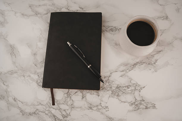 istock A black notebook and a pen rest on a smooth marble surface near a white cup filled with dark coffee, creating a focused and calm workspace in the morning 2254596814