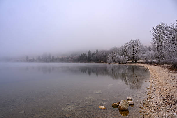 Lago Di Dobbiaco in winter with a perfect reflection, Dolomites, Italy everything is covered with snow and the mist is hanging above the lake.