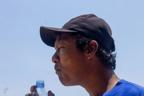 A man is drinking water using a bottle held in his right hand to quench his thirst.
