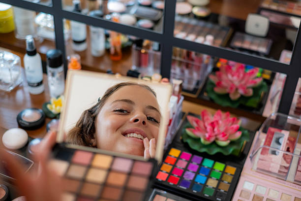 istock Young woman smiling in mirror while applying makeup 2254605032