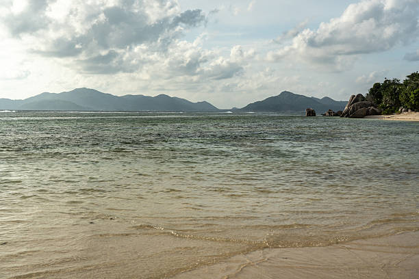 Evening light over Anse Source d Argent beach with granite boulders clear water and view of distant islands on La Digue Island Seychelles