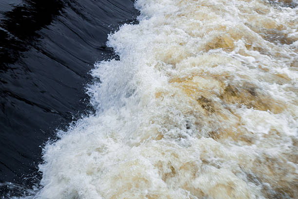 The water is brown and white, with a black edge. The water is crashing against the rocks, creating a powerful and dynamic scene