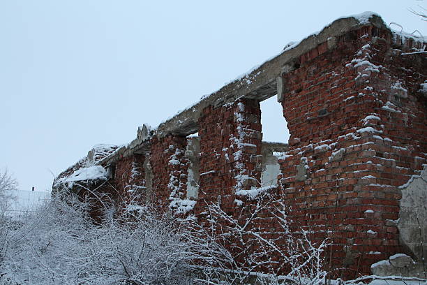 Old abandoned wooden house hidden behind trees in winter village