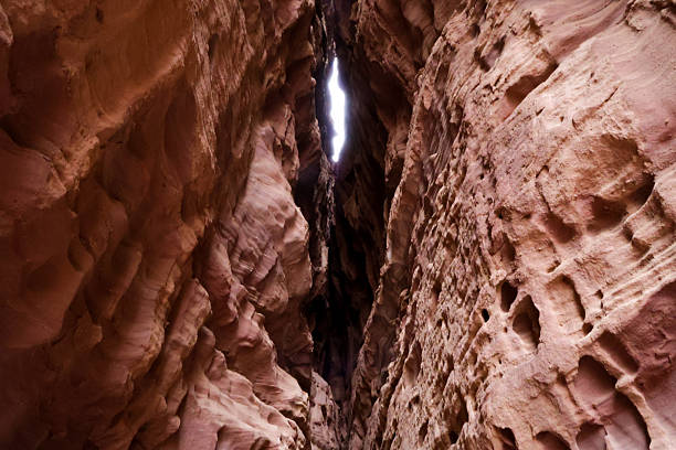 A dramatic, narrow canyon wall scene with pink-red rock and a shaft of light at the top, highlighting rugged textures and natural beauty perfect for nature and adventure themes.