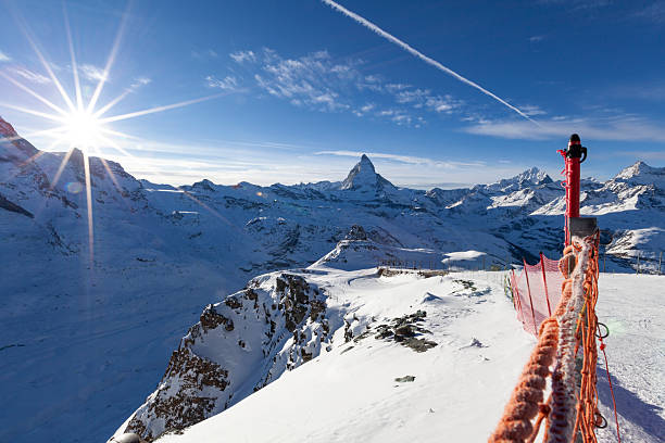 Panoramic winter view from Gornergrat station in the Swiss Alps, featuring the iconic Matterhorn under a clear blue sky. Snow-covered mountains, bright sun rays, and alpine infrastructure create a dramatic high-altitude travel and tourism scene in Switzerland.