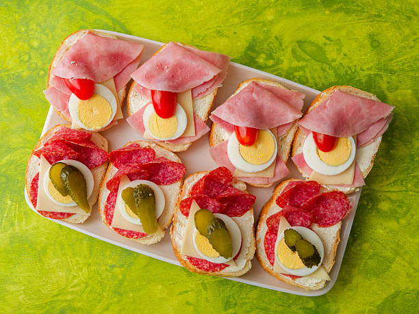 Tasty homemade Czech chlebicky with ham, cheese and salami on tray on green background top view