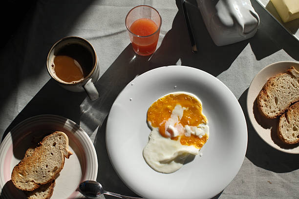 A sunny-side-up egg rests beside a vibrant vegetable medley, crispy bacon, and two golden rolls on a floral-rimmed plate, capturing a simple, hearty breakfast or brunch.