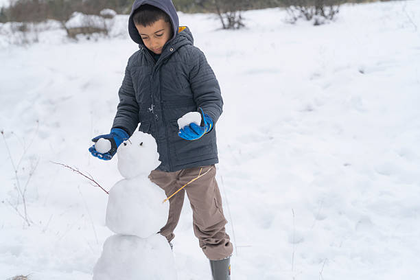 A young child carefully builds a small snowman in a snow-covered landscape, capturing the innocence and creativity of childhood during winter. The peaceful outdoor setting highlights themes of seasonal activities, family life, playful learning, and the simple joy of interacting with nature. Ideal for concepts related to winter holidays, childhood memories, outdoor play, and healthy lifestyles.