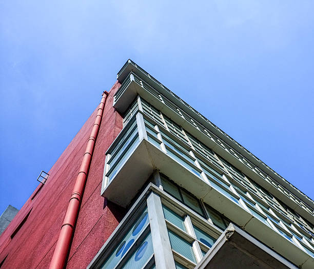 Looking up at the corner of a building exterior against a clear blue sky. The image highlights architectural elements such as cornices, windows, and rooflines. The concept conveys urban design and real estate. Authentic real photography.