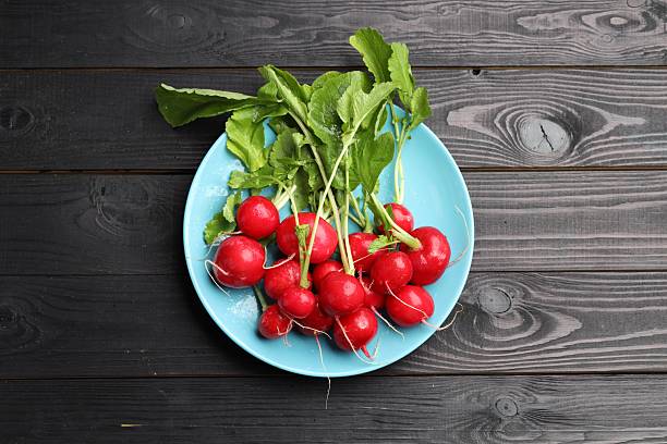 Many fresh radishes on black wooden table, top view