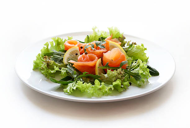 Smoked salmon salad with lettuce, rocket and spinach garnished with lemon slices, pepper and fresh parsley. Fresh and healthy dish. White background. Overhead view.