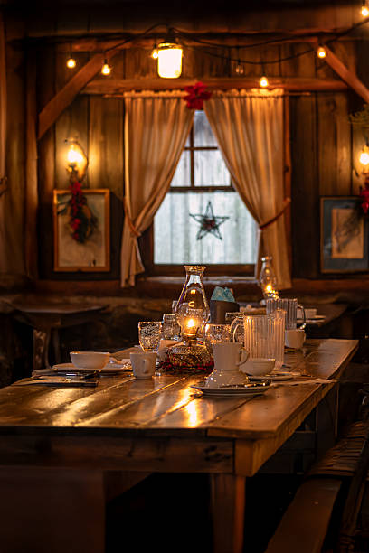 Cozy wooden cabin interior with a set dining table illuminated by oil lamps and warm lights in a winter atmosphere