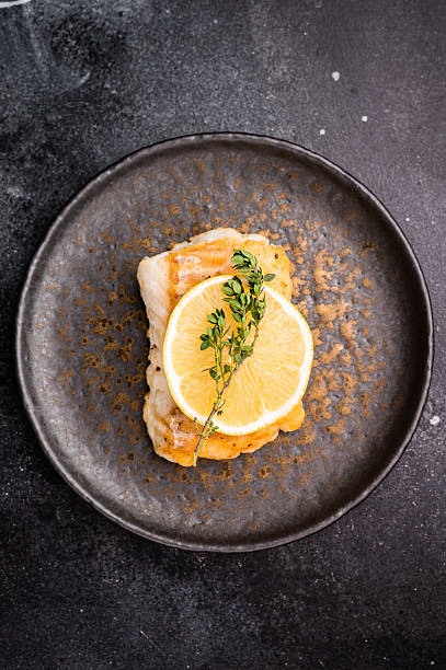 Roast Halibut fish loin fiilet on plate. Black background. top view