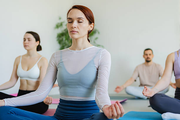 istock Yoga mindfulness meditation. Group of sporty people doing exercise in studio for class for yoga wellness mindfulness meditation. Men women practicing yoga sitting in lotus pose meditating relaxing. 2254644092