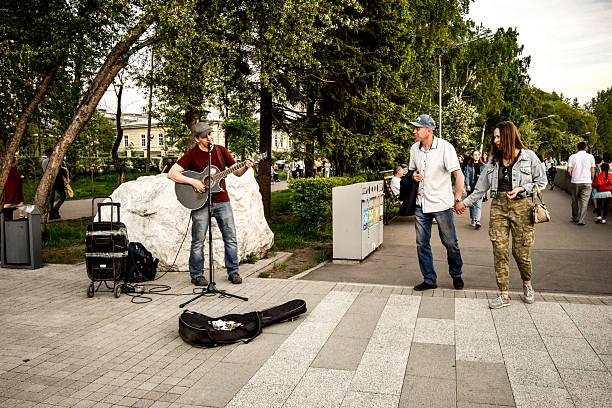 Street guitarist performs music in a public park as a couple walks past during evening leisure time. Irkutsk, Russia, June 5, 2021.