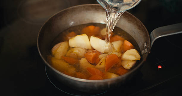 A close-up of water being poured into a frying pan filled with carrot and parsnip, ready to make a hearty stew
