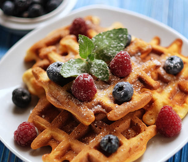 Traditional belgian waffles with fresh berrys and sugar powder on white plate, blue wooden background. Flat lay, top view, copy space. Close up.