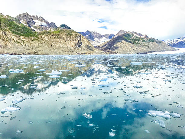 Scenic view of Prince William Sound near Valdez, Alaska, featuring the Chugach Mountains rising above calm waters dotted with floating glacial ice. The mountains are reflected in the surface of the sound, creating a peaceful and awe-inspiring landscape that highlights Alaska’s pristine wilderness and natural beauty.