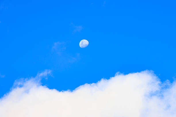 Minimalist sky scene showing the moon visible during daytime against a bright blue sky with soft white clouds. Calm natural background ideal for astronomy, weather, and serenity concepts.