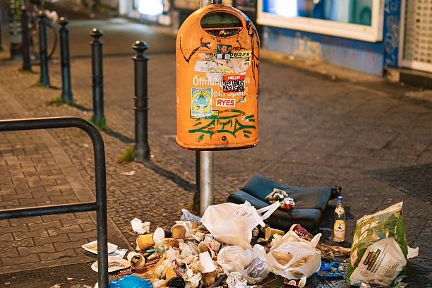 Berlin, Germany – December 28, 2025: Public trash bin surrounded by litter and waste on a sidewalk in the Neukoelln district.