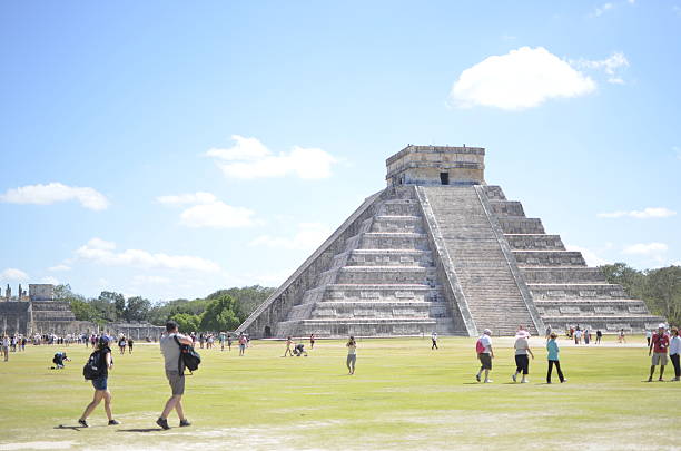 The Chichen Itza archaeological site in Mexico is seen from a distance with visitors walking around the ancient ruins. The image shows the historic landmark and tourism activity at the site. Editorial use only.