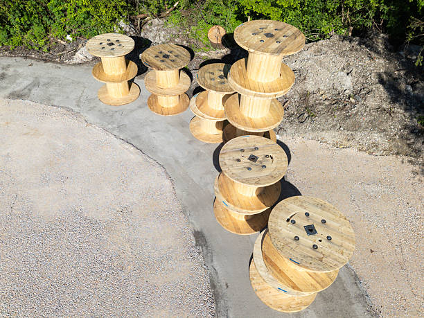 Aerial view of wooden spools stacked on a gravel surface, surrounded by greenery